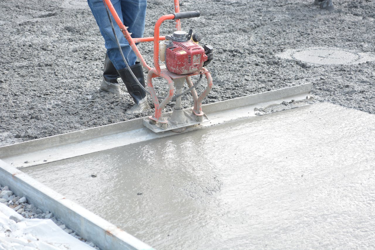 A construction worker operates a power trowel to smooth freshly poured concrete on a construction site.
